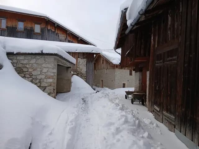 Chemin enneigé entre granges en pierre et vieux mazot en bois